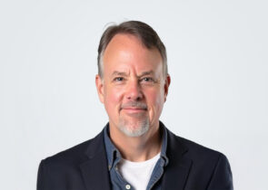 Headshot of a person in a suit jacket with a jean jacket underneath.