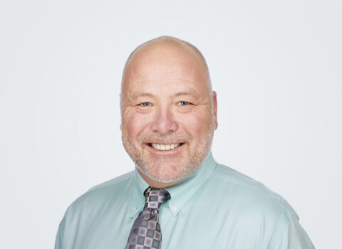 Headshot of Ross Dunning, a man with white hair, in front of a light grey background.