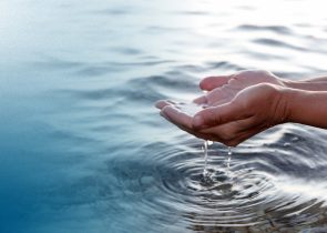 Hands cupping water over a natural body of water