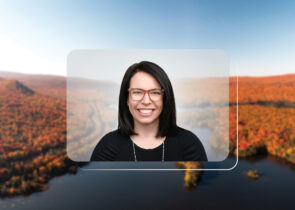 A headshot of Suzanne Broadbent, a woman with brown hair, is centered on top of a photo of a landscape. The landscape setting is in New England. It depicts rolling hills with orange, autumn-colored trees and a blue sky.