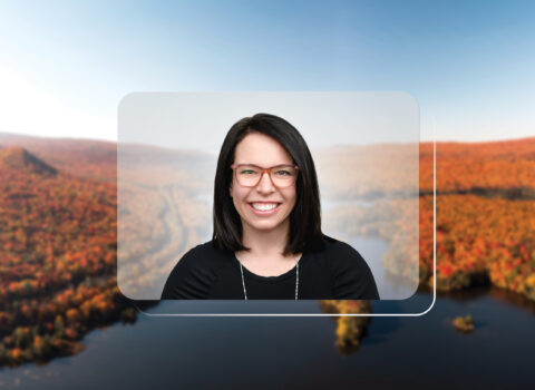A headshot of Suzanne Broadbent, a woman with brown hair, is centered on top of a photo of a landscape. The landscape setting is in New England. It depicts rolling hills with orange, autumn-colored trees and a blue sky.