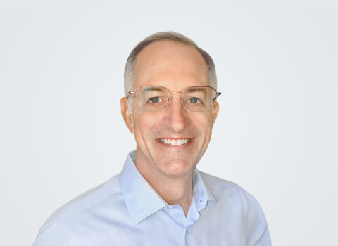 Headshot of Mike Juszynski, a man with brown-white hair, in front of a light grey background.