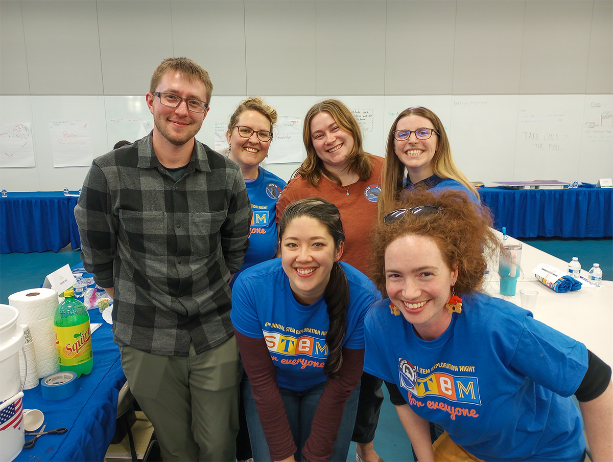 Six KJ employees are shown participating at Federal Way STEM Exploration Night. Four of the employees wear royal blue STEM Exploration Night shirts.
