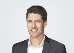 Headshot of Michael Humm, a person with short, dark brown hair, wearing a charcoal suit.