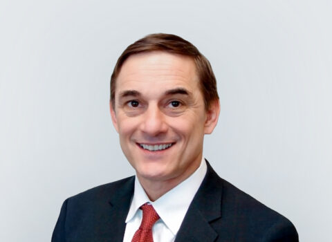 Headshot of a person with short brown hair, suit jacket, and red tie.