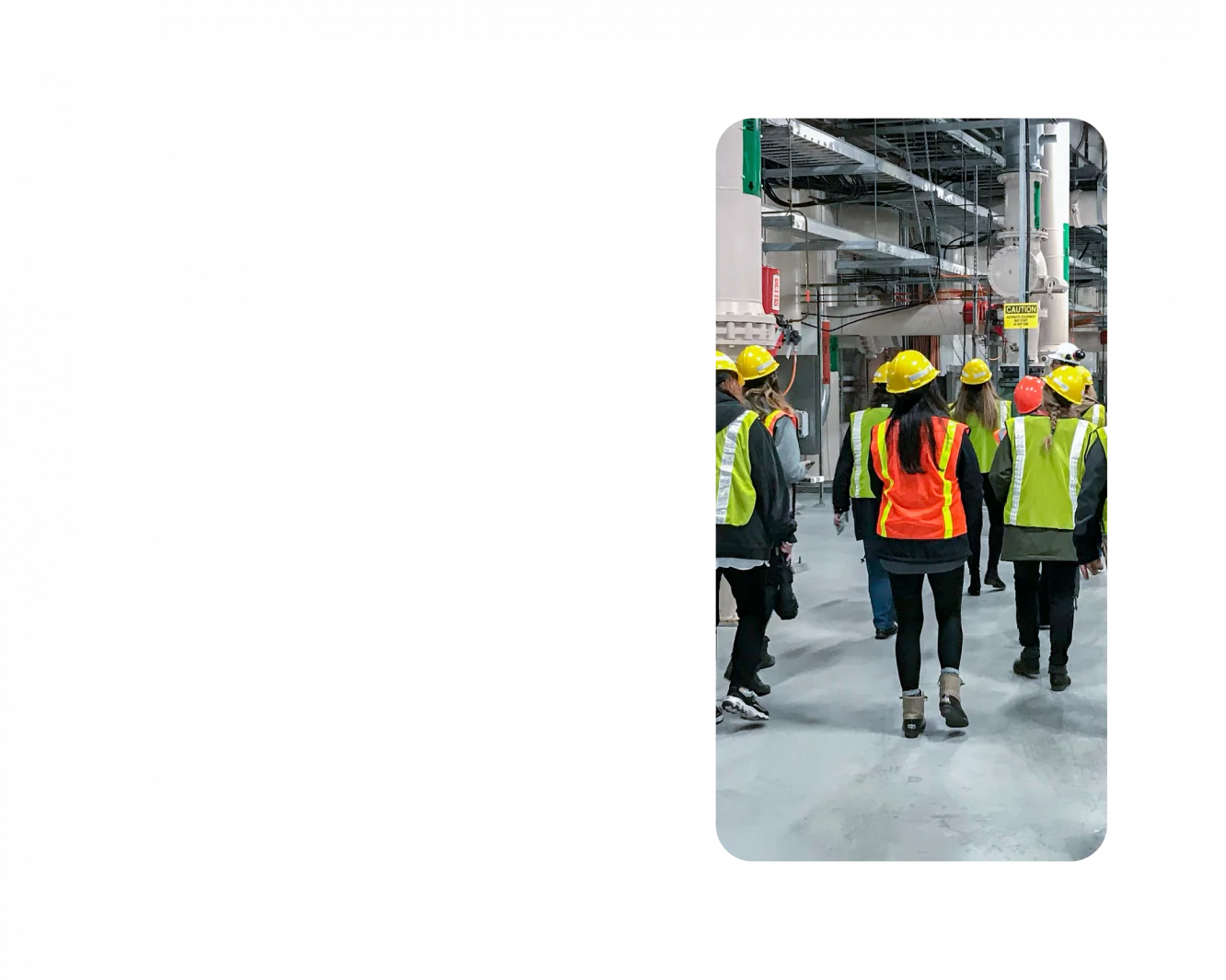 A group of KJ employees tour a water management facility. They are wearing fluorescent orange, yellow, and green safety vests and hard hats.