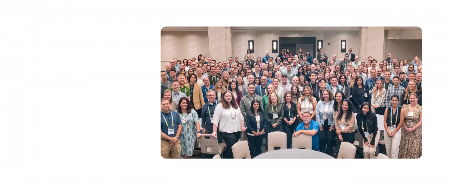 A large group of KJ employees pose for a photo at TechEx 2024. The employees are dressed in business casual clothing and stand in a cream-colored banquet room.
