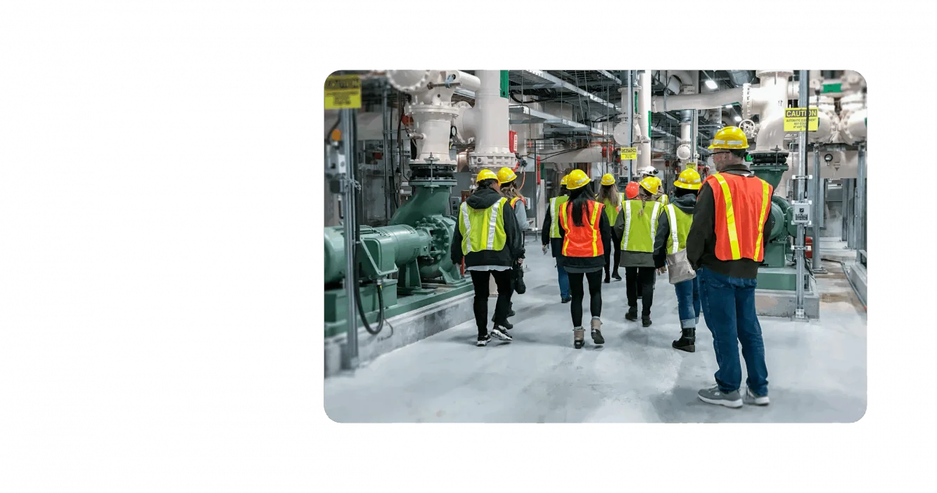 A group of KJ employees tour a water management facility. They are wearing fluorescent orange, yellow, and green safety vests and hard hats.