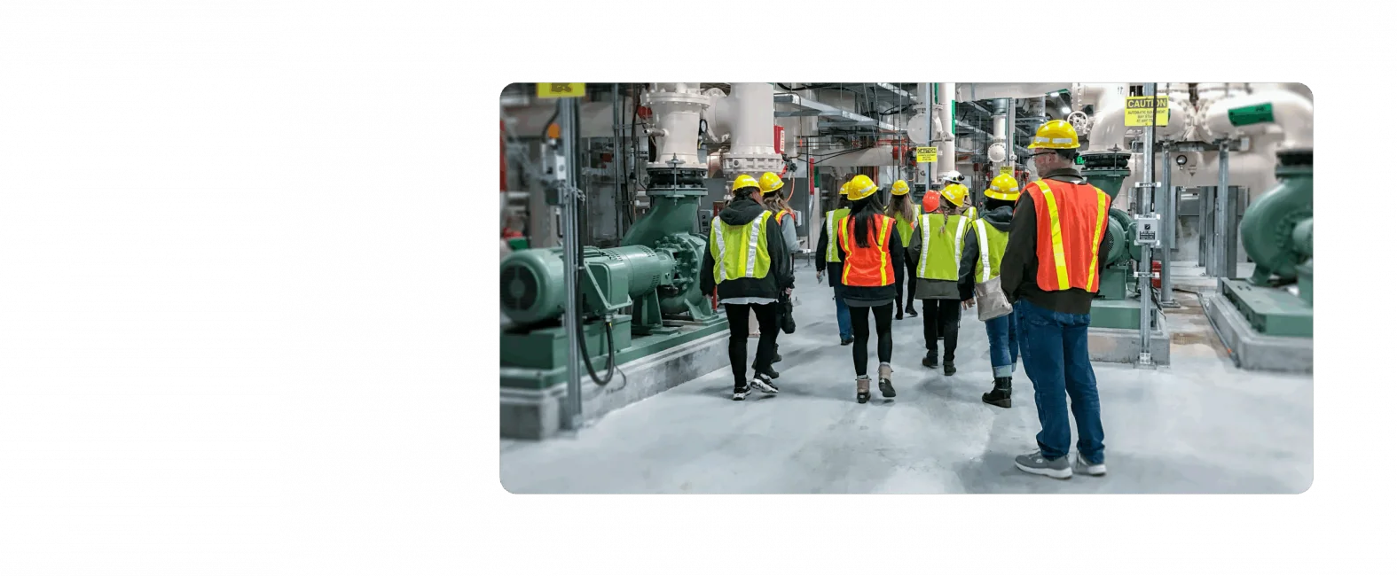A group of KJ employees tour a water management facility. They are wearing fluorescent orange, yellow, and green safety vests and hard hats.