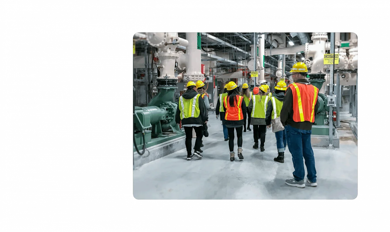 A group of KJ employees tour a water management facility. They are wearing fluorescent orange, yellow, and green safety vests and hard hats.