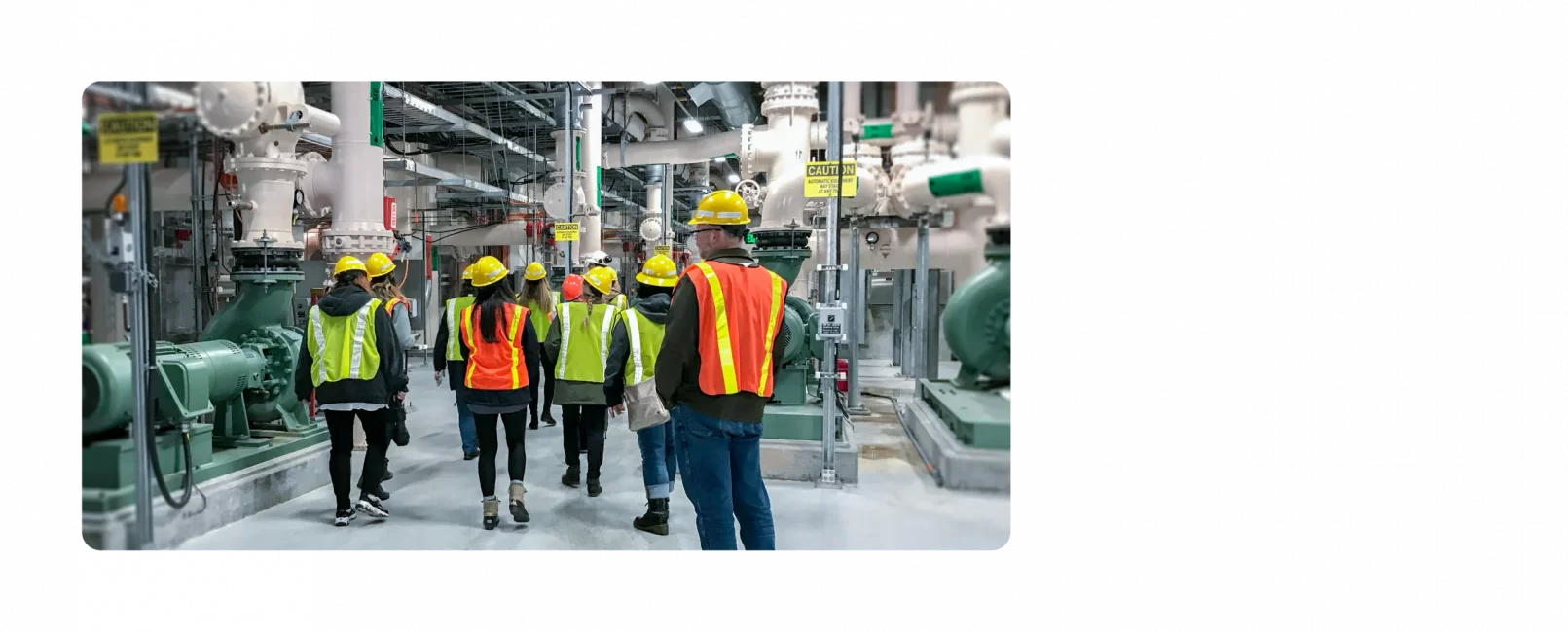 A handful of KJ employees walk through a water facility. They are wearing dark clothes with neon hard hats and neon vests on top.