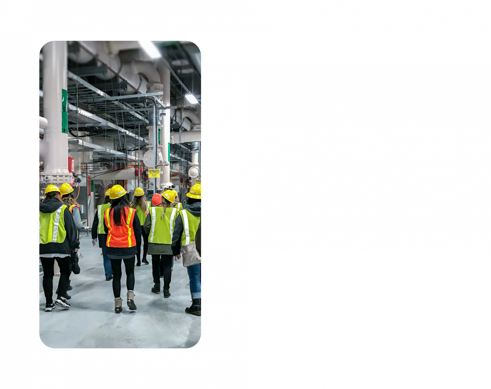 A handful of KJ employees walk through a water facility. They are wearing dark clothes with neon hard hats and neon vests on top.